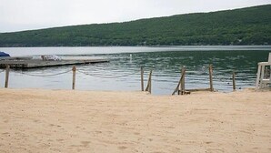 A sandy beach with a wooden dock extending into calm water, surrounded by green hills.