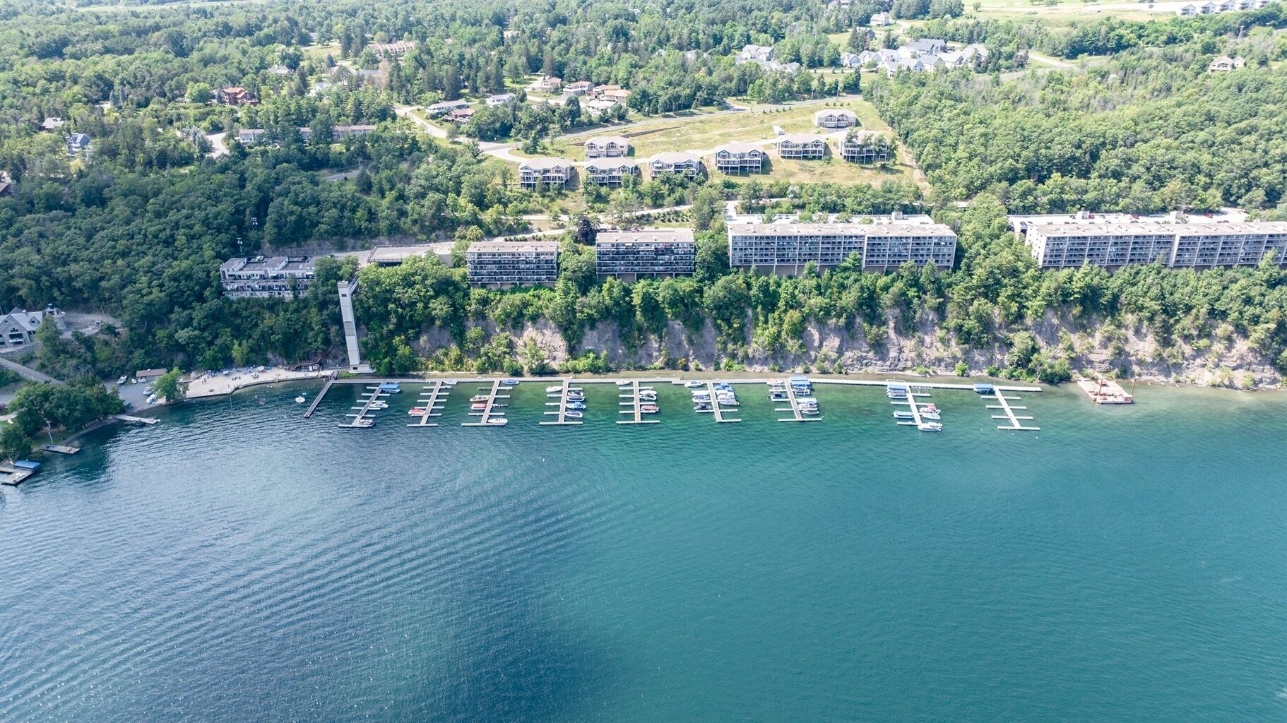 Vista aérea de una propiedad frente al agua con varios edificios, un puerto deportivo con barcos y vegetación circundante.
