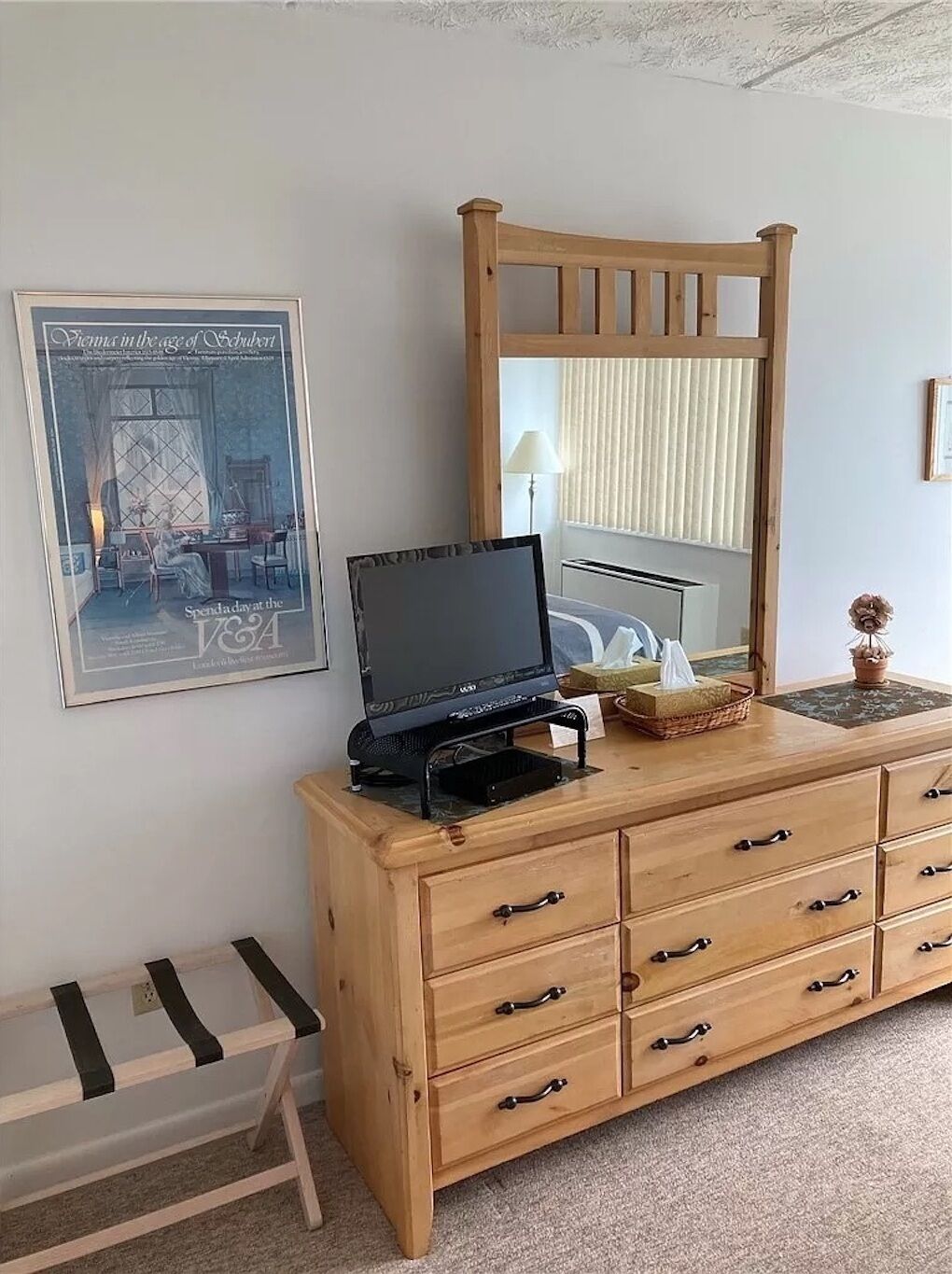 A bedroom with a wooden dresser, a mirror, a framed picture, and a small table with a lamp.