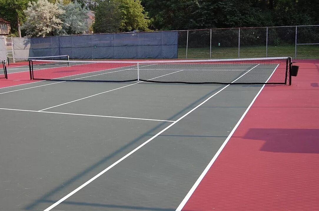 A tennis court with a net, surrounded by a fence and trees.