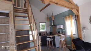 A modern kitchen with a wooden staircase, a dining area with bar stools, and a large mirror on the wall. - Lovely, cosy little chalet close to a wood (Montardon)