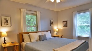 Ein ordentlich bezogenes Bett mit blauer Bettdecke und Kissen, zwei Nachttischlampen und gerahmte Bilder an den Wänden.