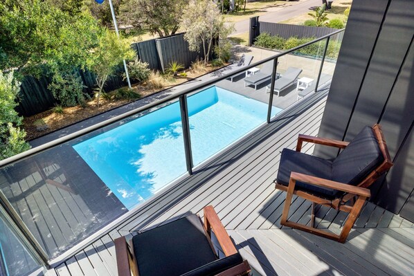 Relax on the balcony with a clear view of the pool, surrounded by lush greenery.