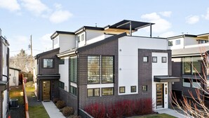 Una casa moderna de dos pisos con techo plano, ventanas grandes y un pequeño jardín delantero.