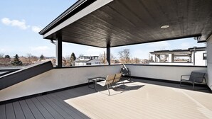 Una terraza en la azotea con diseño moderno, que cuenta con un piso de madera y sillas de metal.