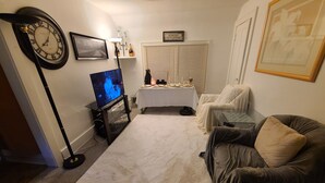 Ein Wohnzimmer mit Fernseher, einer Uhr, einem Tisch mit Dekoration und einer Couch.