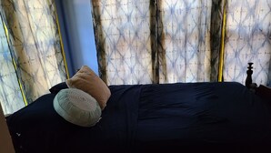 Ein Bett mit dunkelblauer Bettdecke und zwei Kissen, eines grün, eines beige, in einem Zimmer mit gemusterten Vorhängen.