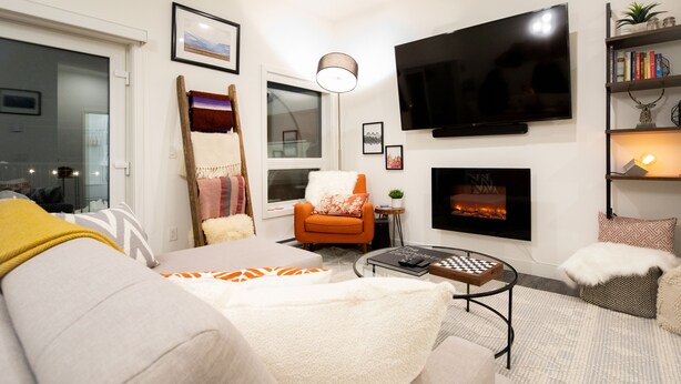 Una sala de estar moderna con un sofá, un sillón, chimenea, televisor de pantalla plana y una estantería.