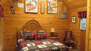Camera accogliente in legno con un letto di legno, una ventola a soffitto e arredamento rustico, tra cui poster di film e un cartello di Kern's Bread.