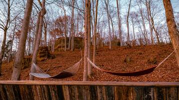 A hammock set up between two trees in a forested area with a wooden deck in the foreground.