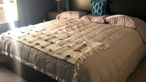 Ein Schlafzimmer mit einem großen Bett, einem Nachttisch mit Lampe, einem Deckenventilator und einem Fenster mit Jalousien.