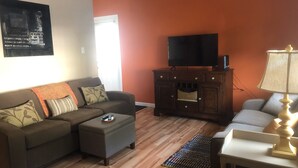 Ein Wohnzimmer mit Sofa, Hocker, Fernsehschrank und einer Lampe.