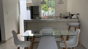 A modern kitchen with a central island, white chairs, and a glass dining table. - Casa Puerta del Sol ☀️Cozy 2bedroom Wifi. AC and TV (Mérida)