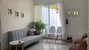 A modern living room with a grey sofa, two white chairs, a small round table, and a potted plant. - Casa Puerta del Sol ☀️Cozy 2bedroom Wifi. AC and TV (Mérida)