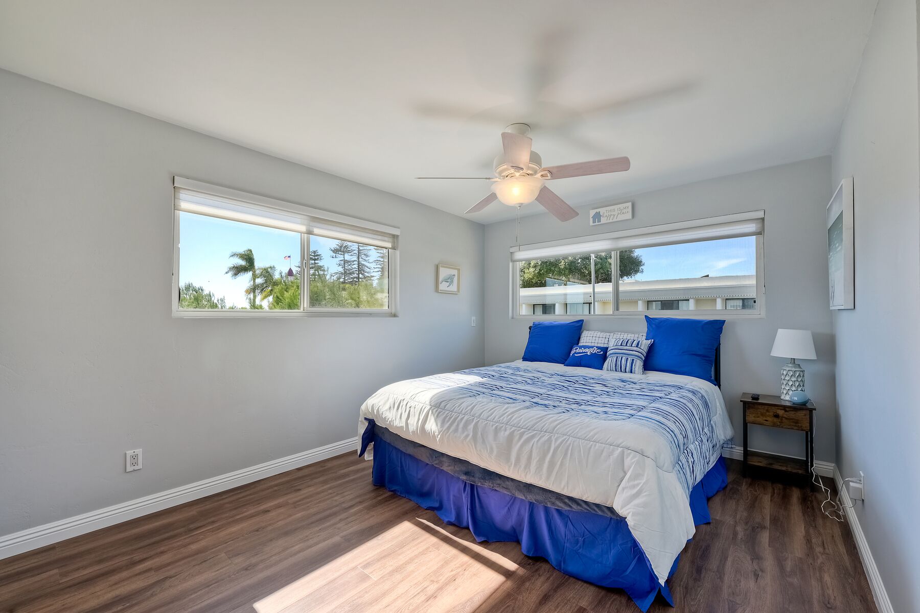 A bedroom with a bed, two windows, a ceiling fan, and a nightstand.