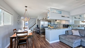 A modern kitchen with a central island, stainless steel appliances, and a dining area with wooden chairs and a chandelier. - *NEW*Fantastic Location! Large Balcony Overlooking Yacht Club. Walk to Hotel Del (Coronado)