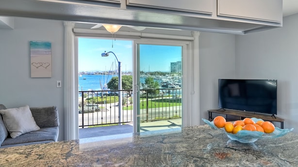 A modern kitchen with a large window, a bowl of oranges on the counter, and a TV on a wooden stand. - *NEW*Fantastic Location! Large Balcony Overlooking Yacht Club. Walk to Hotel Del (Coronado)