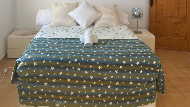 A neatly arranged bedroom with a bed, pillows, a hanging light fixture, and a wall-mounted air conditioner. - Studio in a private estate in the center of the island (Sant Llorenç)