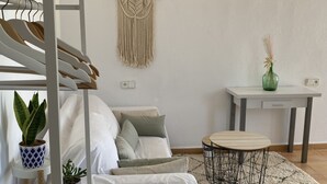 A modern living room with a white sofa, a round wooden coffee table, a macrame wall hanging, and a small green vase on a white table. - Studio in a private estate in the center of the island (Sant Llorenç)
