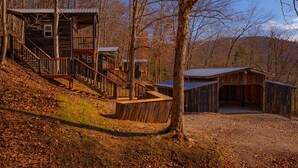 A rustic cabin with a wooden staircase leading to a deck, surrounded by trees and a clear sky. - Glamping Cabin | Huge Window | Tree House Feel (Green Township)