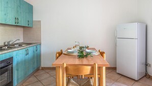 Eine kleine Küche mit türkisfarbenen Schränken, einem Holztisch und einem weißen Kühlschrank.