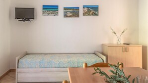 Ein kleines Zimmer mit einem Bett, einem an der Wand montierten Fernseher und drei gerahmten Bildern mit Küstenmotiven.