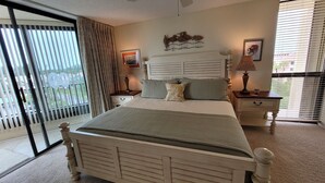 Quarto com uma cama grande, duas mesas de cabeceira com abajures, um ventilador de teto e vista para o exterior por uma porta de vidro deslizante.