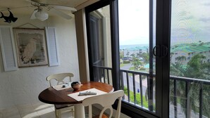 Uma área de refeições com mesa e cadeiras, um ventilador de teto, um quadro e vista para uma área residencial por grandes janelas.