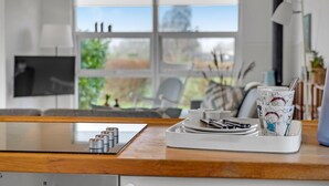 A kitchen with a modern stove, a window with a view of greenery, and a tray with plates and utensils. - 3 bedroom awesome home in Egernsund (Egernsund)