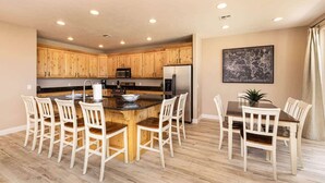 A modern kitchen with wooden cabinets, a central island with seating, and a dining area with chairs.