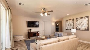 A living room with a beige sofa, a coffee table, a television, and a ceiling fan.