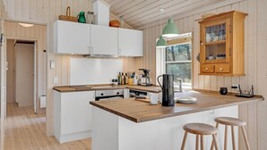 Een moderne keuken met witte kasten, een houten eiland, barstoelen en uitzicht op de omgeving door een raam.