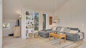 Een gezellige woonkamer met een grijze bank, een houten salontafel en een witte boekenkast vol boeken en decoratieve spullen.