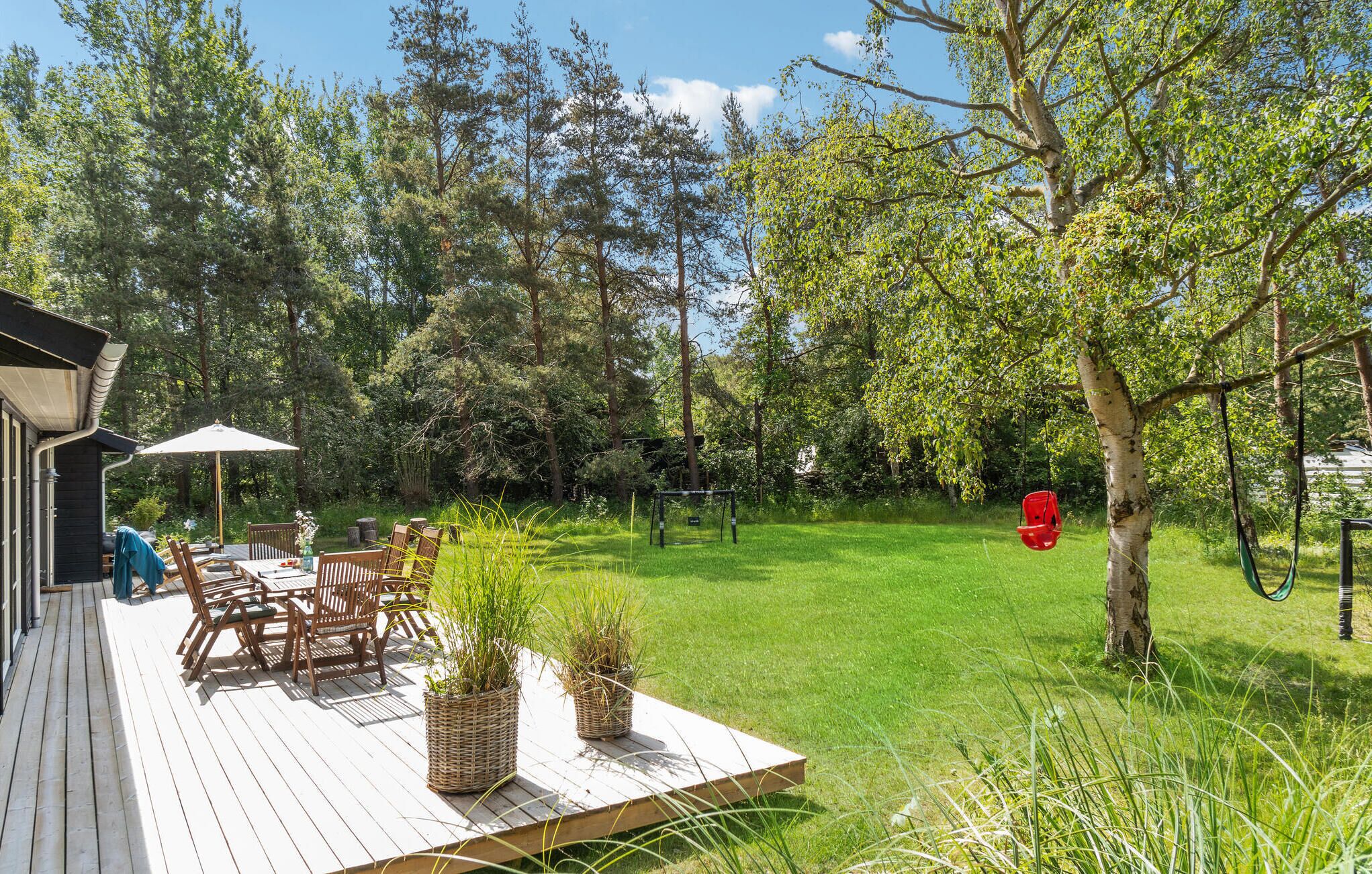 A wooden deck with outdoor furniture, a swing set, and a grassy yard surrounded by trees.
