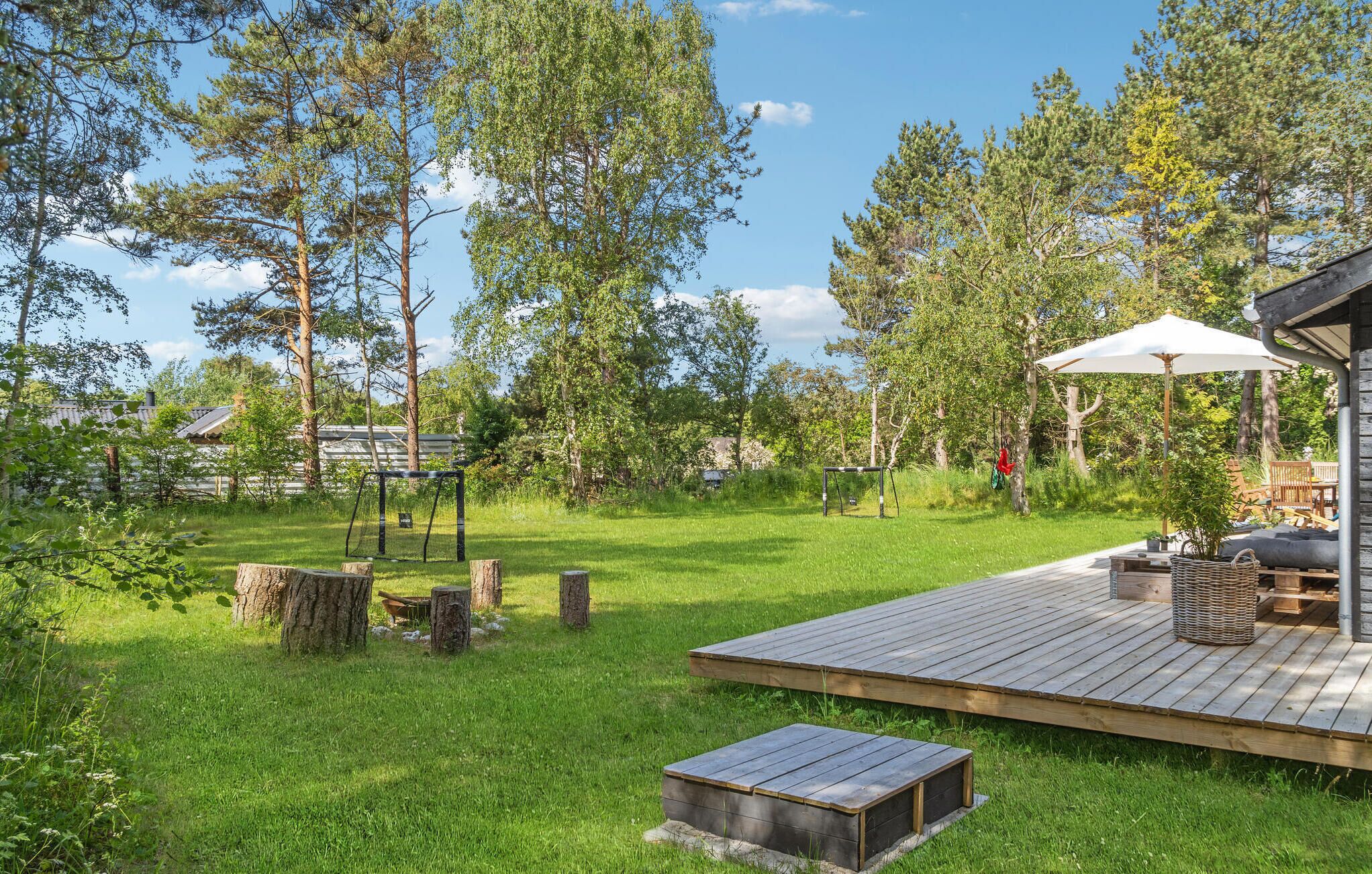Une terrasse en bois avec une table et des chaises, entourée d’une pelouse et d’arbres.