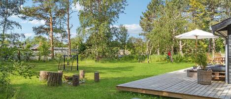 Une terrasse en bois avec une table et des chaises, entourée d’une pelouse et d’arbres.