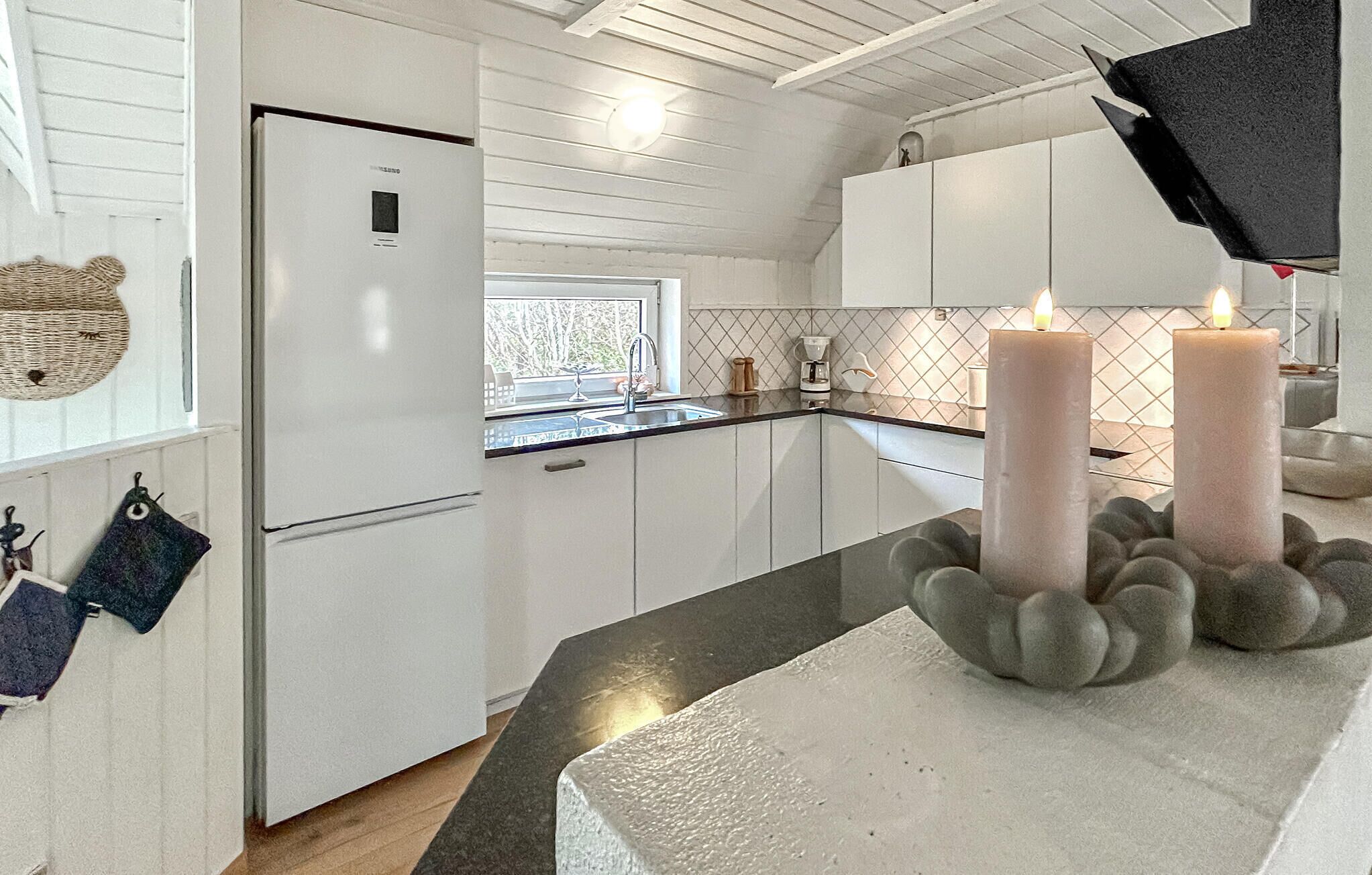 A modern kitchen with white cabinets, a built-in refrigerator, and a window with a view of trees.