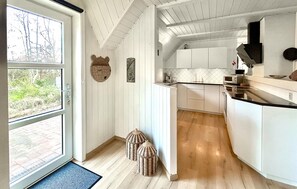 A kitchen with white cabinets, a microwave, and a coffee maker. There are wicker baskets on the floor and a window with a view of trees.