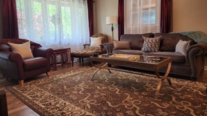 Un salon avec un canapé marron, un fauteuil marron, une table basse en verre et un tapis à motifs.