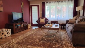 Un salon avec un téléviseur, des canapés, une table basse et un tapis à motifs.