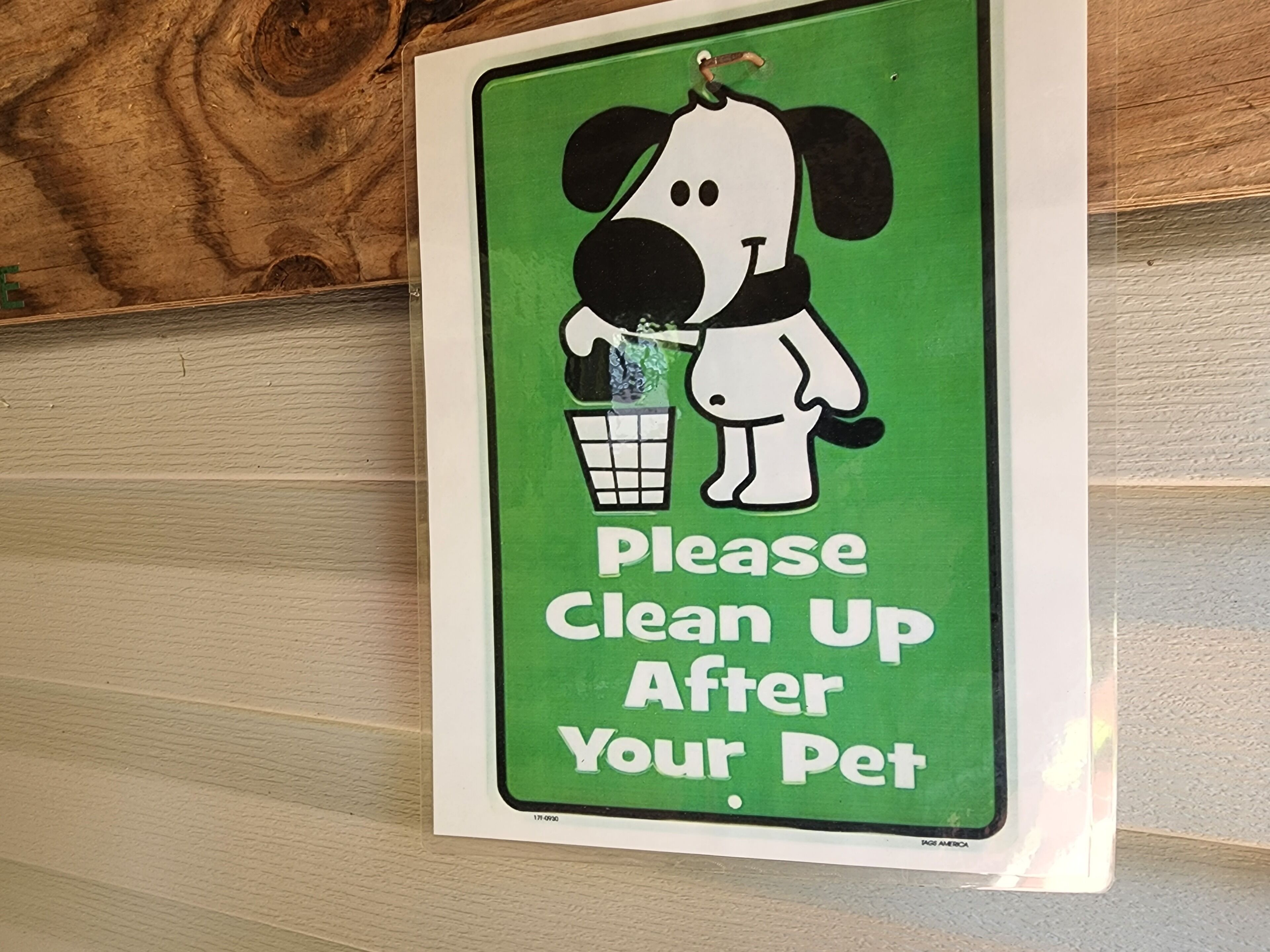 Un letrero verde con un perro caricaturesco sosteniendo un cono de helado y el texto 'Please Clean Up After Your Pet'.
