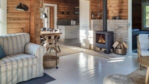 Ein gemütliches Blockhaus-Interieur mit einer Couch, einem Esstisch, einer Küchenzeile und einem Kaminofen.