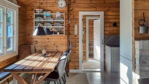 Ein Holzblockbau-Innenraum mit Esstisch, Stühlen, einer Uhr und einer Küchenzeile.