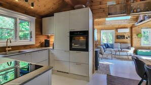 Eine moderne Küche mit weißen Schränken, einem eingebauten Backofen und einer Kaffeemaschine. Ein Essbereich mit einer Couch und einem Tisch ist ebenfalls vorhanden.