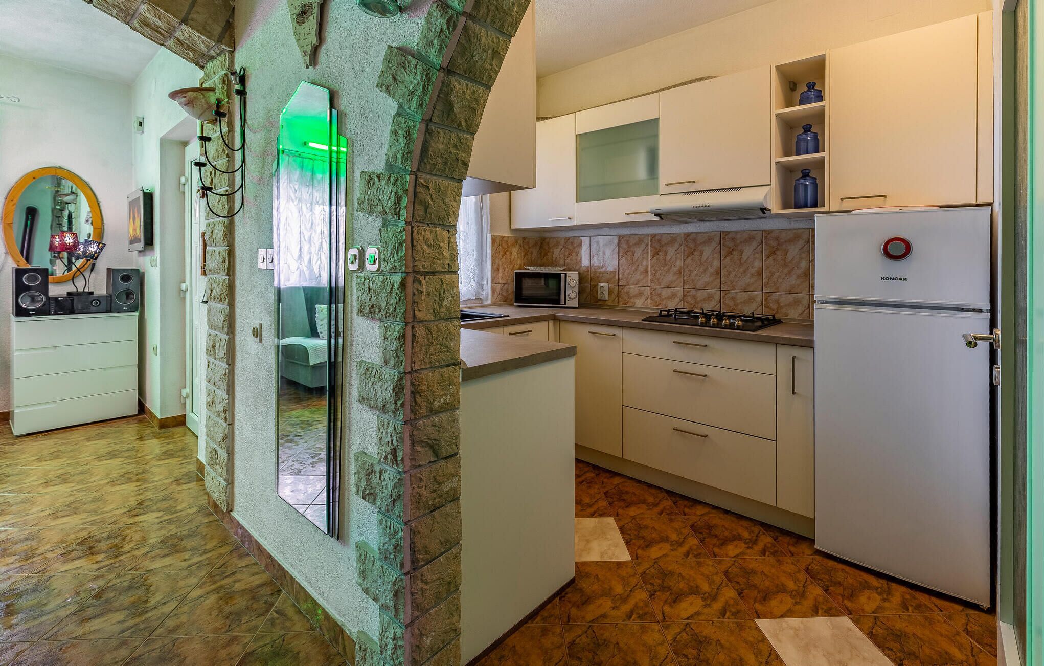 A compact kitchen with a microwave, stove, and a refrigerator. There is a stone wall with a glass door leading to another room.