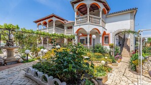 Un bâtiment à deux étages doté d’un balcon, d’un chemin en pierre et de diverses plantes.