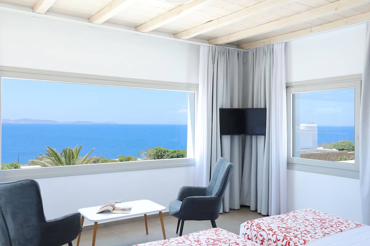 Une pièce dotée d’une grande fenêtre donnant sur la mer, d’un téléviseur à écran plat, d’une petite table et de deux chaises.