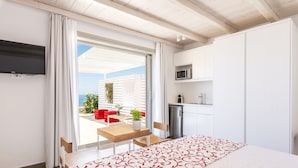 Une chambre d’hôtel moderne équipée d’un lit, d’une télévision, d’une kitchenette et d’un balcon avec une table et des chaises.