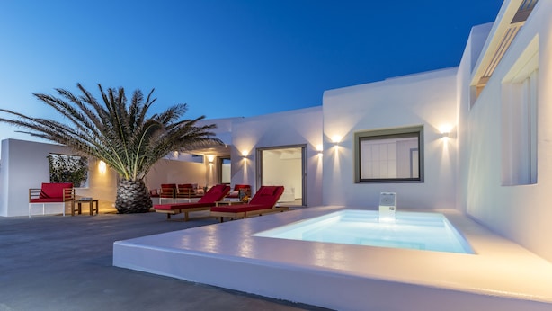 Un espace piscine extérieur moderne, avec des chaises longues rouges, un palmier et un intérieur bien éclairé.