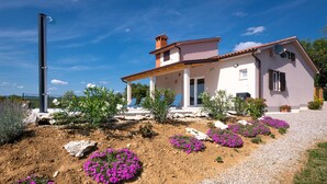 A two-story house with a patio area, surrounded by a garden with purple flowers and a gravel path. - Beautiful home in Krsan (Krsan)